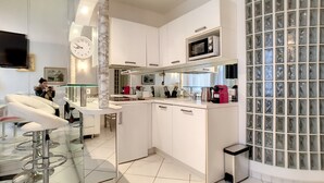 A modern kitchen with white cabinets, a microwave, a coffee machine, and a glass backsplash. - HENRI CAMILLE AGENCY- Croisette - 2 bedrooms, 2 Bathrooms, 50m Croisette (Cannes)