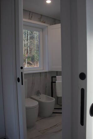 Un baño moderno con inodoro, bidé y ventana con vistas a árboles.