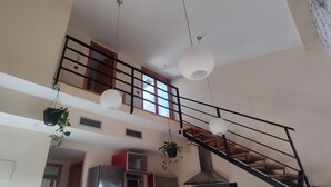 A spacious interior with a high ceiling, a staircase with a wooden railing, and hanging plants. - MIRADOR DEL TORREÓN (Alcañiz)