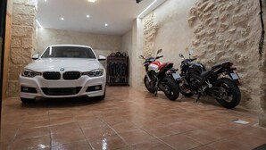 A white BMW car parked in a garage with two motorcycles and a shoe rack. - MIRADOR DEL TORREÓN (Alcañiz)