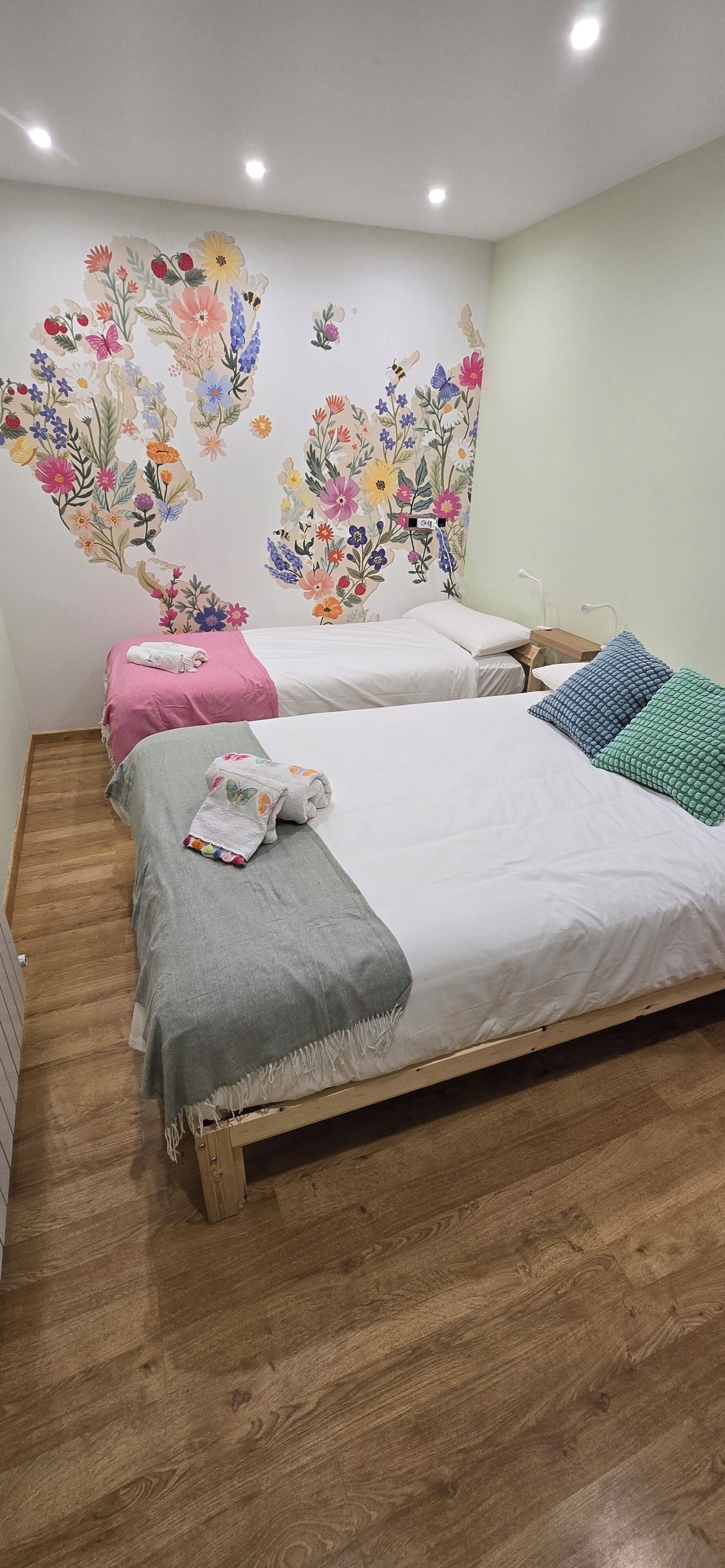 A bedroom with two beds, wooden flooring, and a floral mural on the wall.