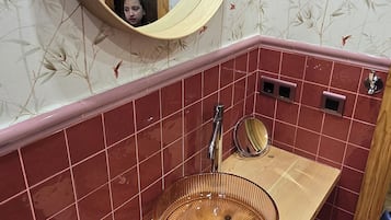 A bathroom with a round mirror, a wooden vanity, a sink with a circular basin, and red-tiled walls.