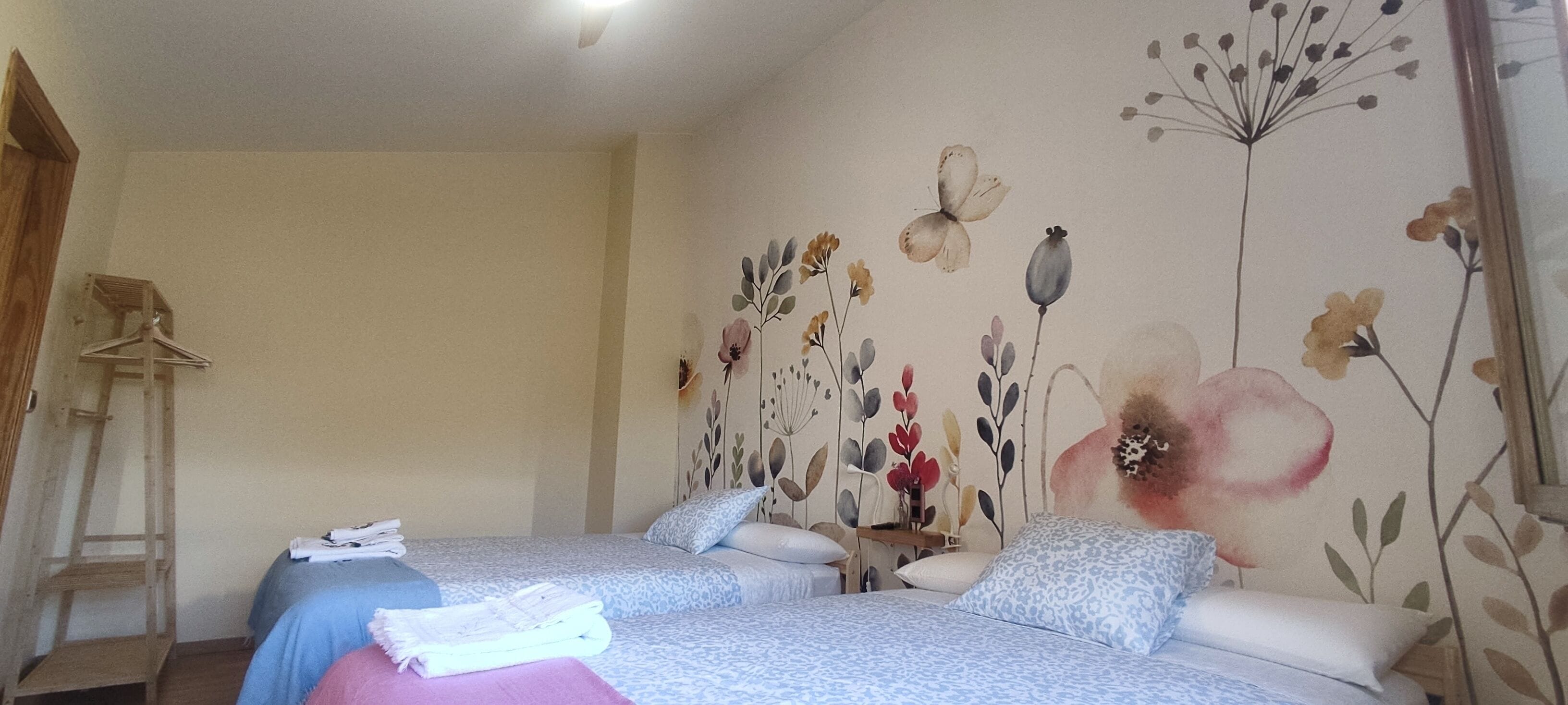 Un dormitorio con dos camas, una escalera de madera y un muro con motivos florales.