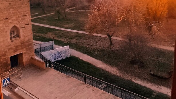 A view from a window overlooking a sunset, a stone building, and a grassy area with a path. - MIRADOR DEL TORREÓN (Alcañiz)
