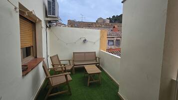 A small balcony with a green artificial turf, wooden furniture, and a string of lights.