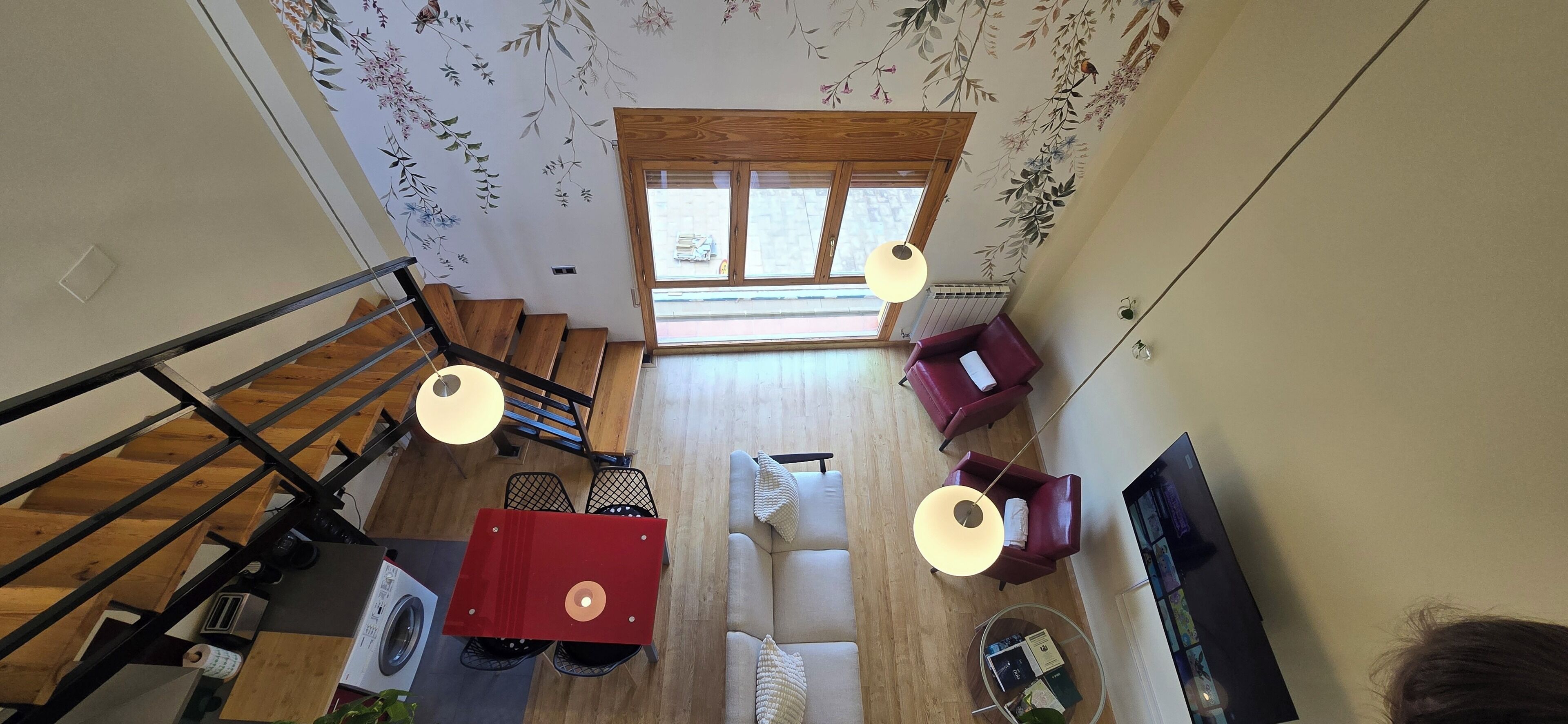 A spacious living area with a staircase, a red table, a sofa, and a TV.