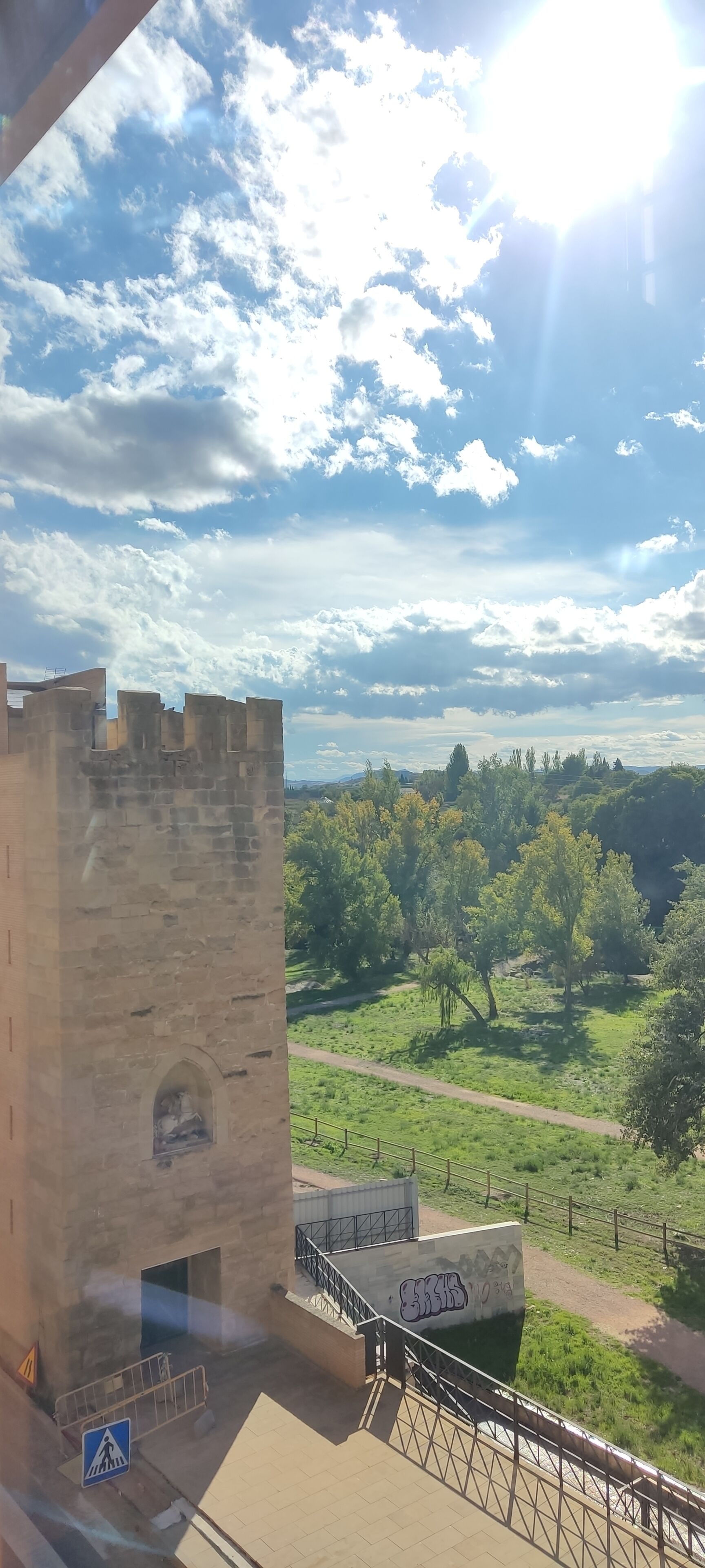Una torre de piedra, un área cercada y un camino que lleva a un paisaje verde.