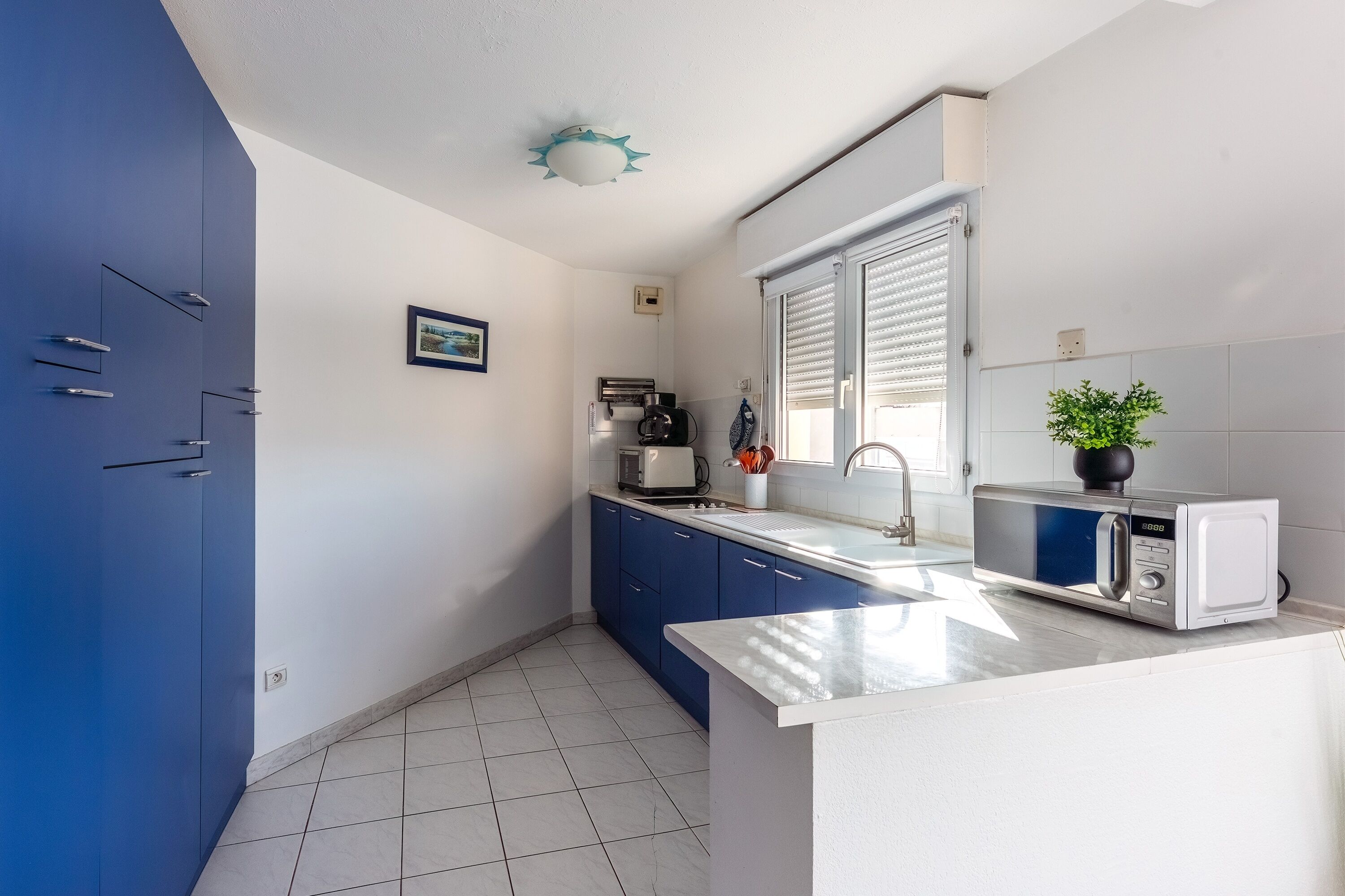 Een moderne keuken met blauwe kastjes, een wit aanrecht en een magnetron.