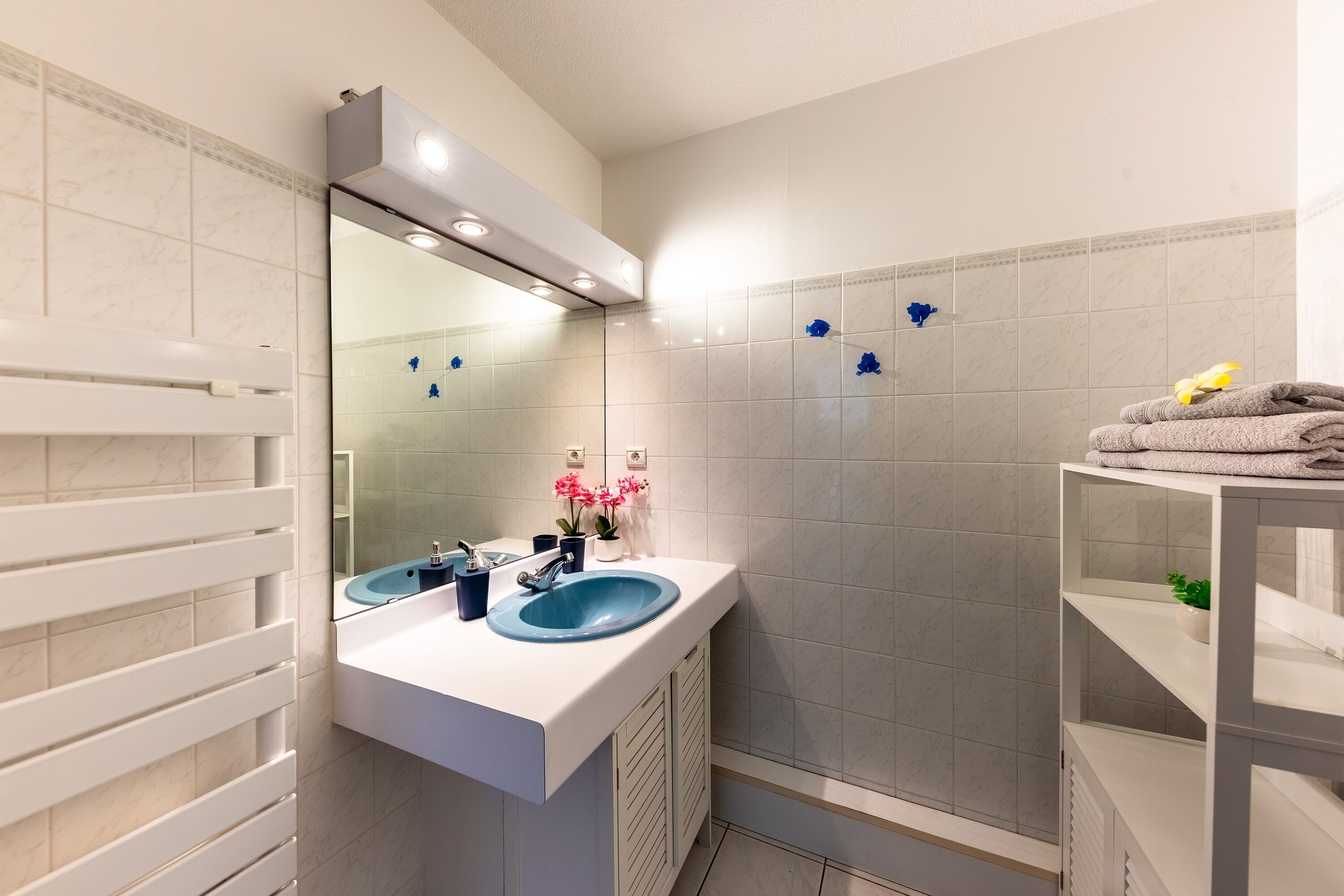A bathroom with a white vanity, two sinks, a mirror, and a shower area.