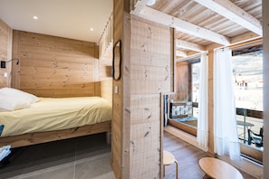 A wooden interior with a bed, a small table, and a window with a view of a snowy landscape. - Le 337 - Antares - Au pied des pistes (Villarembert)