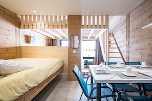 Ein Zimmer in einer Holzhütte mit einem Bett, einem Esstisch für vier Personen und einer Treppe.