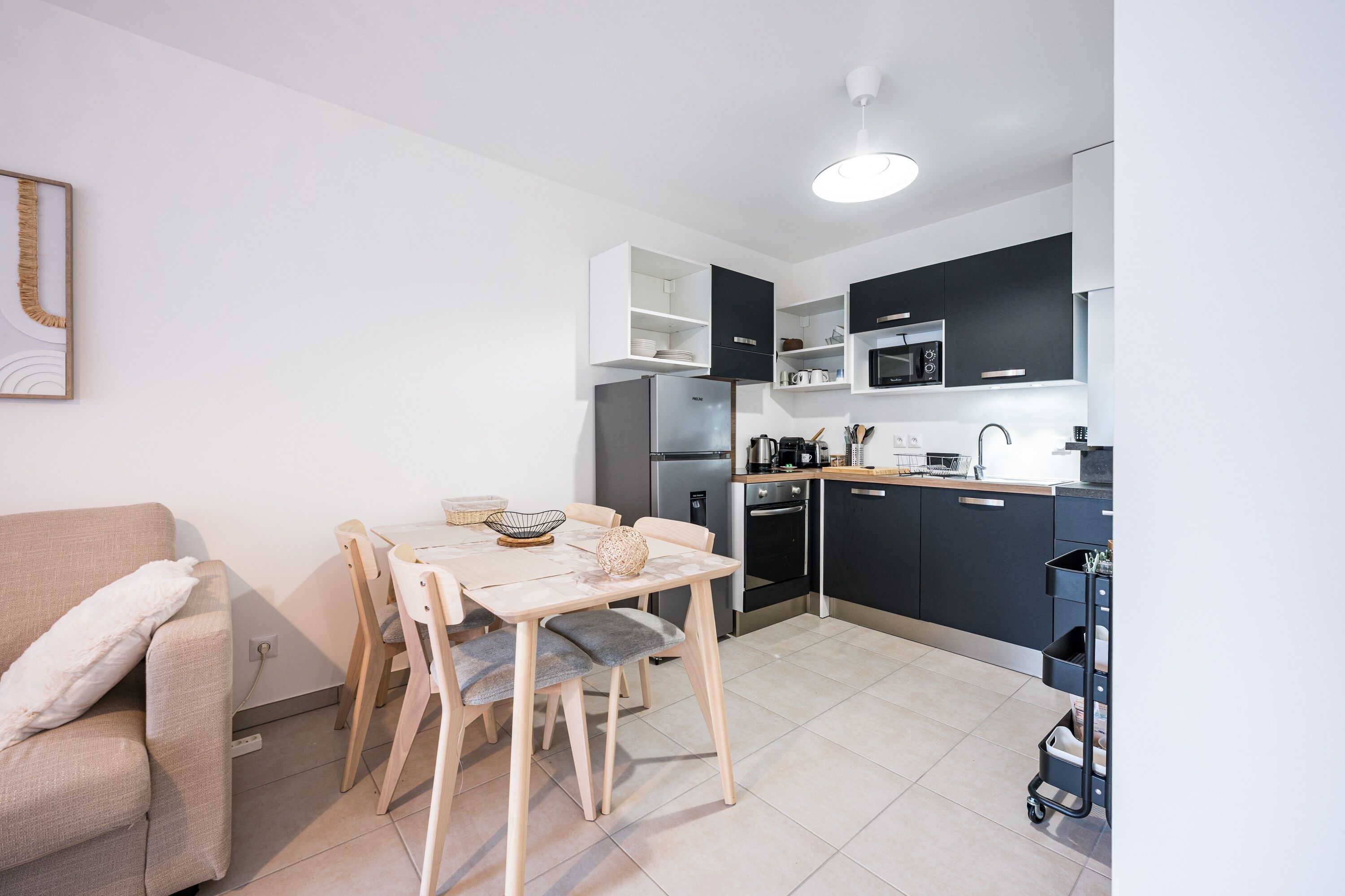 Une cuisine moderne avec des meubles de rangement blancs et foncés, un réfrigérateur, un four à micro-ondes et un four traditionnel. On y trouve une table à manger avec des chaises et une petite table basse.