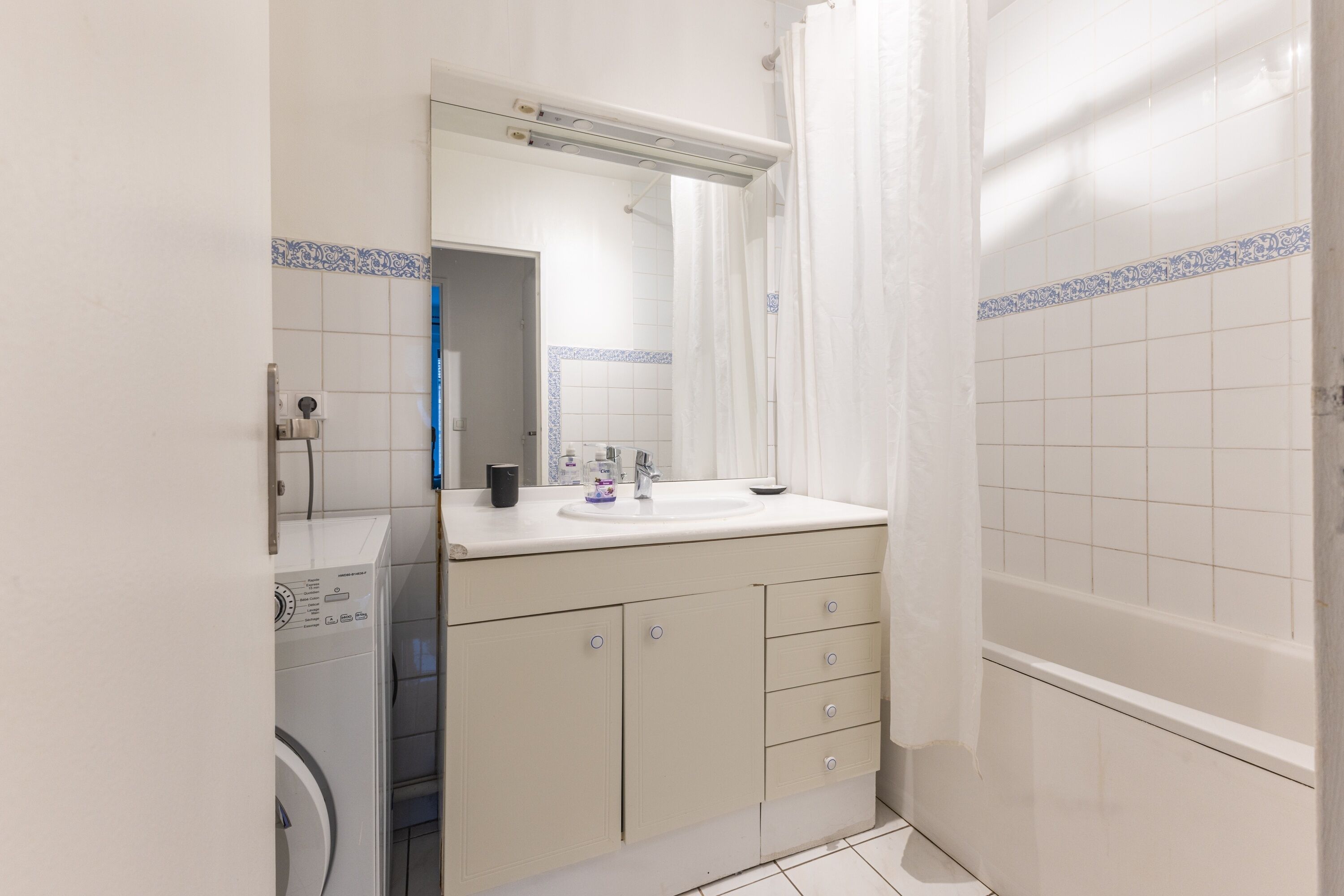Uma casa de banho compacta com máquina de lavar roupa, lavatório com espelho e banheira.