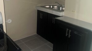 Une petite cuisine équipée d’un évier, de placards et d’une fenêtre agrémentée d’un rideau à motifs floraux.