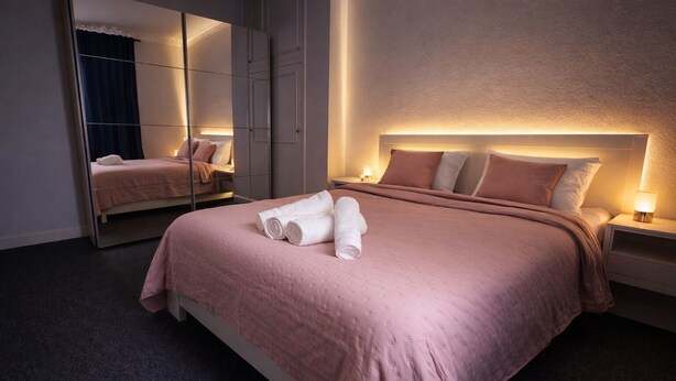A modern hotel room with a large bed, a mirror, and a nightstand with a lamp.