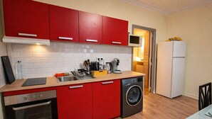 A compact kitchen with red cabinets, a built-in oven, a washing machine, and a microwave.