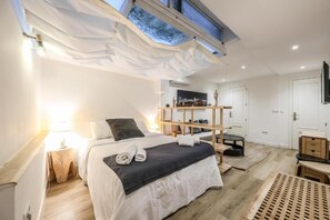 Een moderne slaapkamer met dakraam, een bed met donker hoofdbord, een houten plank en een klein tafeltje.
