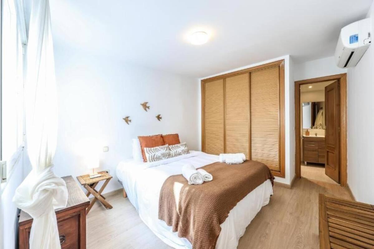 A bedroom with a bed, a wooden wardrobe, a small bedside table, and a window with curtains.