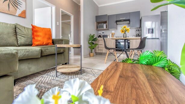 Una sala moderna con una mesa de centro de madera, un sofá con cojines naranjas y un comedor con una mesa y sillas de madera.