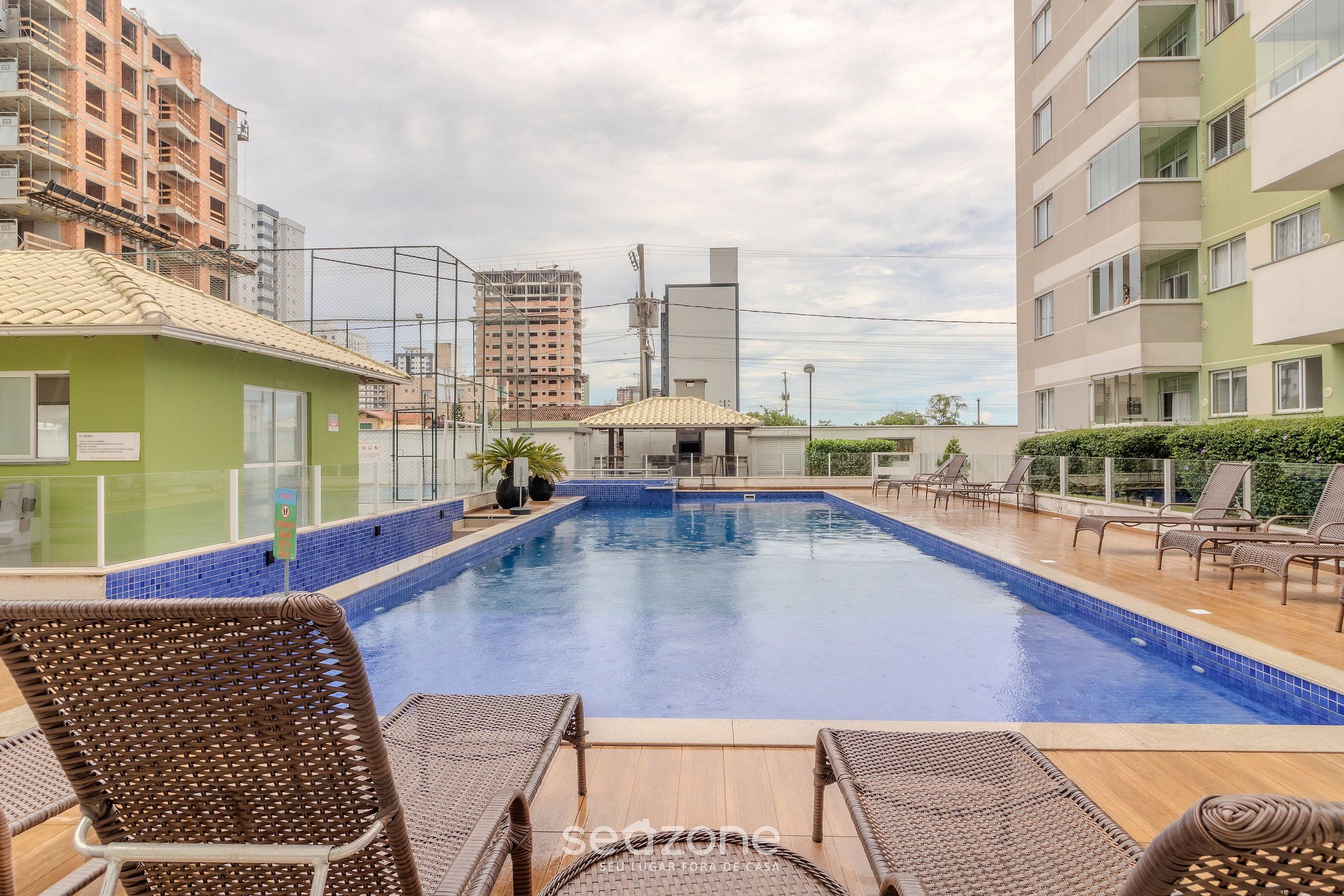 Piscina com espreguiçadeiras e um pequeno pavilhão, cercada por edifícios.