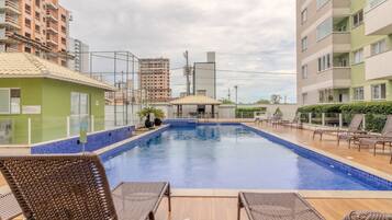 Piscina com espreguiçadeiras e um pequeno pavilhão, cercada por edifícios.