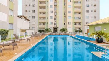 Piscina com espreguiçadeiras e um edifício ao fundo.