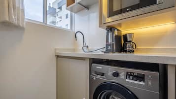 A compact kitchen with a washing machine, a coffee maker, and a microwave.