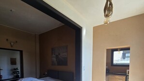 Ein Schlafzimmer mit einem Bett, einem Esstisch und einer durch eine geöffnete Tür einsehbarer Küchenbereich.