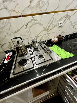 A kitchen with a gas stove, a kettle, and a green cloth on the countertop. - Quiet apartment in Awrir (Agadir)
