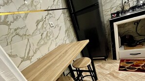 Eine Küche mit Marmorfliesenspiegel, einem schwarzen Kühlschrank, einem Holztisch mit zwei Hocker und einem Fliesenboden.