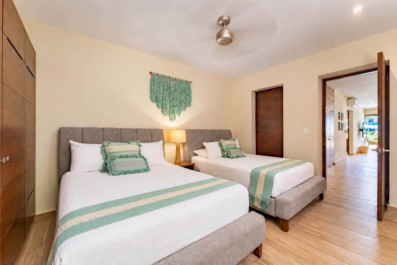 A hotel room with two beds, a wall hanging, and a hallway leading to another room.
