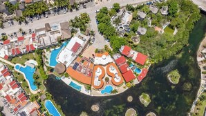 Ovenfra ses et resort med flere swimmingpools, en central bygning med rødt tag og et vandareal omkring.