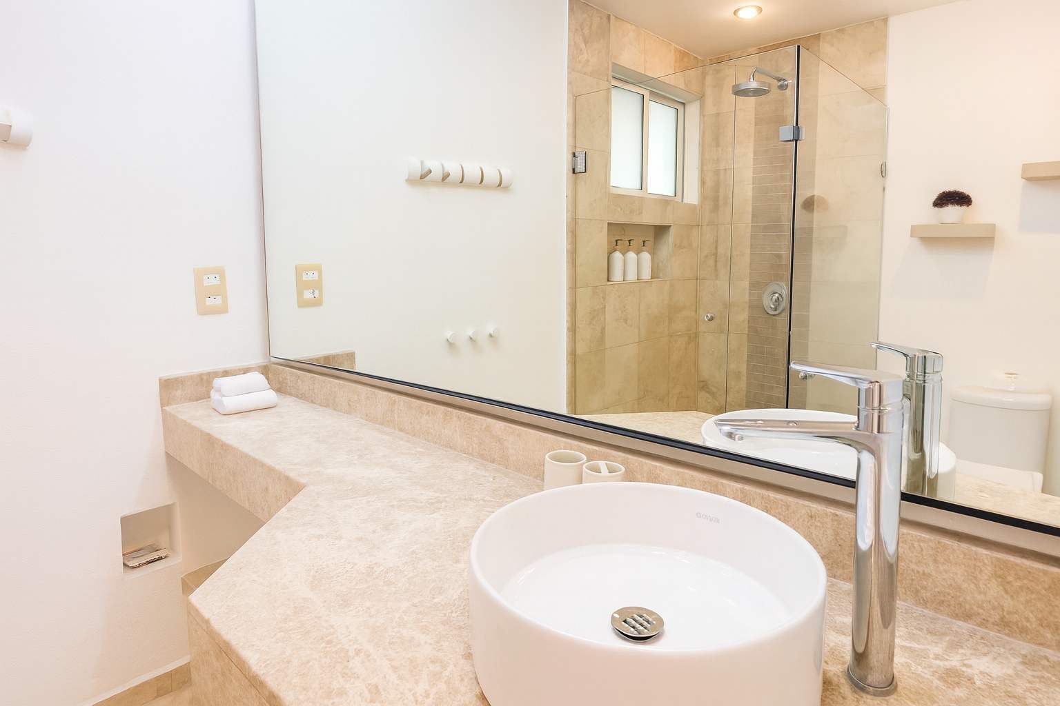 A modern bathroom with a large mirror, a round sink, and a glass-enclosed shower.