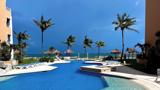 A pool area with clear blue water, lounge chairs, and palm trees. - Beachfront|PrivateHotTube|Grill|Groundfloor (Puerto Aventuras)