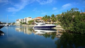 A marina with a large yacht, calm water, and buildings with balconies and palm trees. - Beachfront|PrivateHotTube|Grill|Groundfloor (Puerto Aventuras)