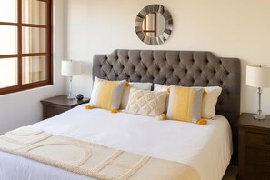 A neatly arranged bedroom with a tufted headboard, a large mirror, and a bed with white bedding and decorative pillows. - Private Jacuzzi Villa in Cabo (Cabo San Lucas)