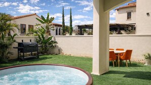 Un jardin avec un jacuzzi, un barbecue et un coin repas agrémenté de chaises orange.