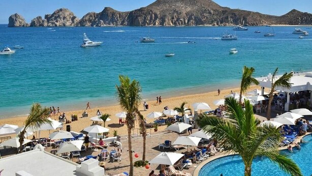 Un complexe hôtelier de bord de mer avec une piscine, des parasols et des bateaux en arrière-plan.
