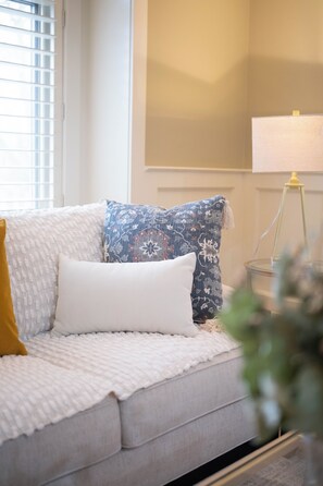 A sofa with a white and mustard-colored throw blanket, a white pillow, and a blue patterned pillow.