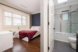 Ein Schlafzimmer mit einem Bett, einem Nachttisch und einem Fenster. Der Raum hat Holzböden und eine weiße Tür.