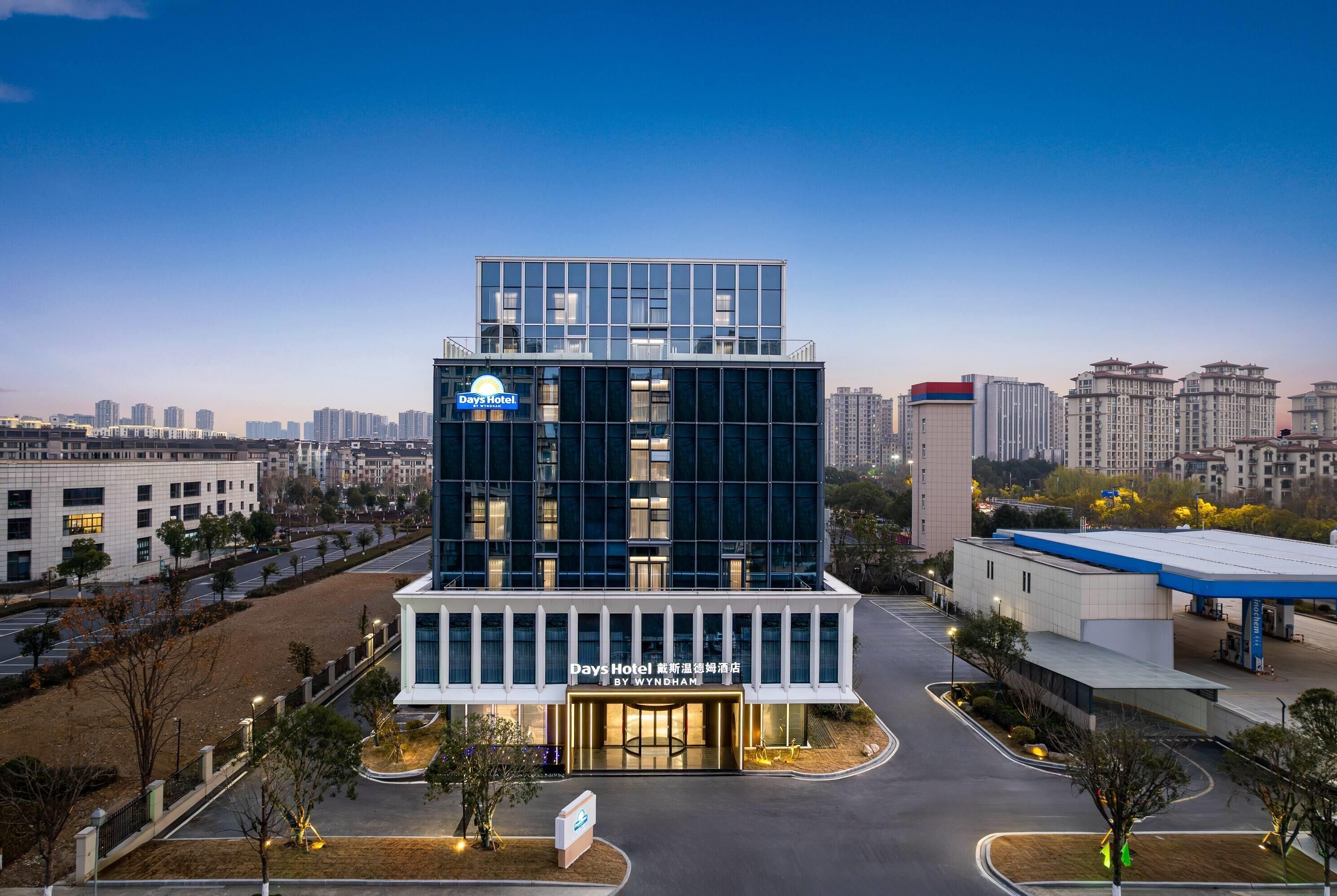 A modern hotel with a glass facade, a sign indicating it's a Wyndham hotel, and a well-maintained parking area.