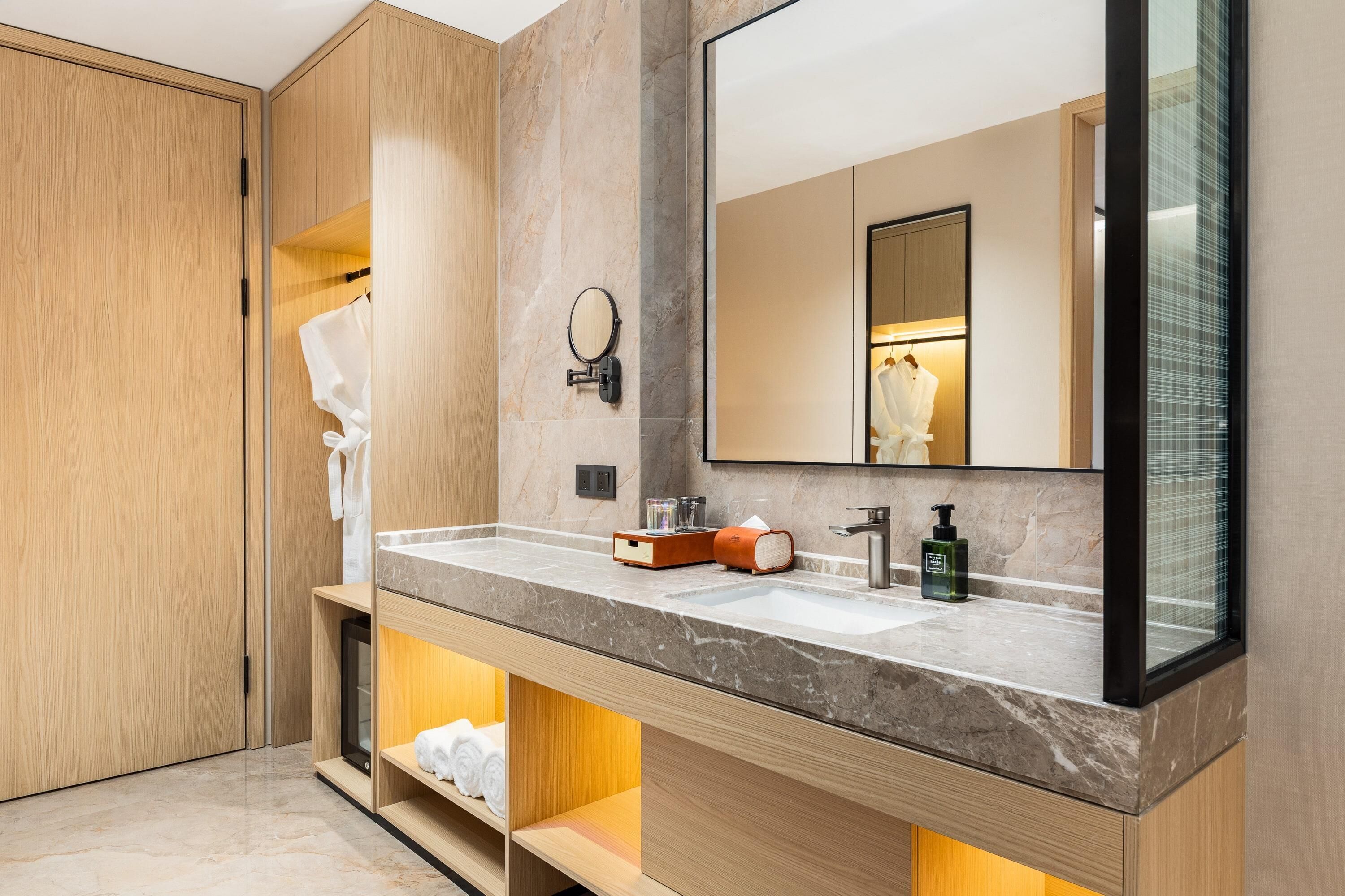 Un baño moderno con muebles de madera, encimera de mármol, un espejo grande y estanterías empotradas.