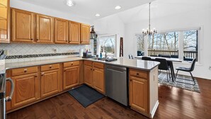 A kitchen with wooden cabinets, a dishwasher, and a dining area with a view. - One-level w/FirePit, 2 Living Areas & Resort Amens (Hedgesville)