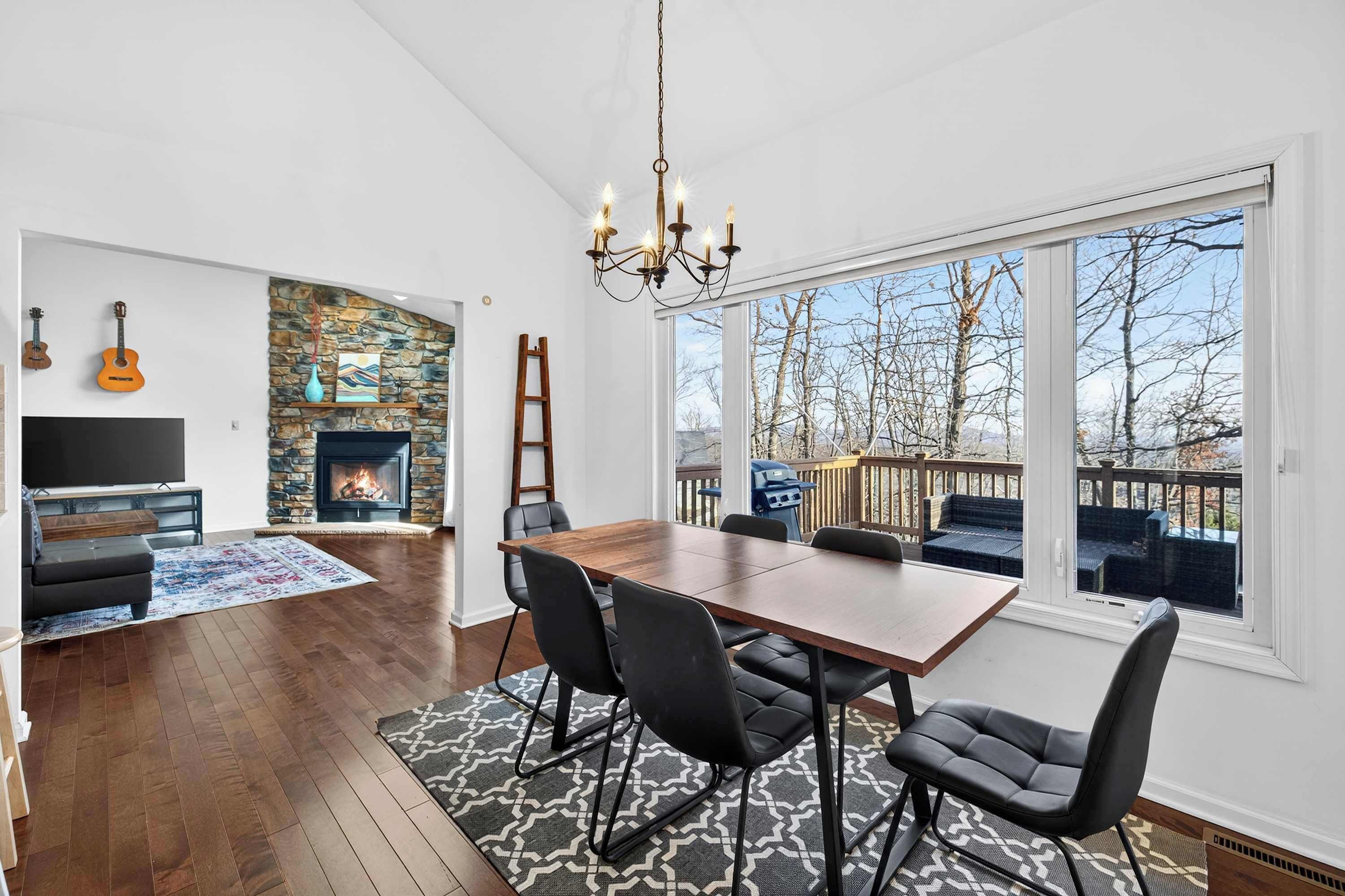 A spacious living room with a fireplace, a dining area with a large table and chairs, and a view of the outdoors through large windows.