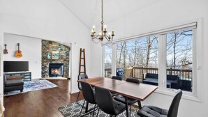 A spacious living room with a fireplace, a dining area with a large table and chairs, and a view of the outdoors through large windows. - One-level w/FirePit, 2 Living Areas & Resort Amens (Hedgesville)