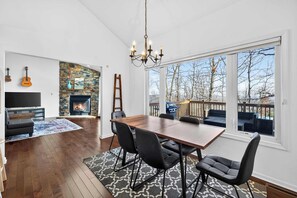 A spacious living room with a fireplace, a dining area with a large table and chairs, and a view of the outdoors through large windows. - One-level w/FirePit, 2 Living Areas & Resort Amens (Hedgesville)