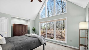 A bedroom with a large bed, a window with a view of trees, a wooden cabinet, and a lamp. - One-level w/FirePit, 2 Living Areas & Resort Amens (Hedgesville)