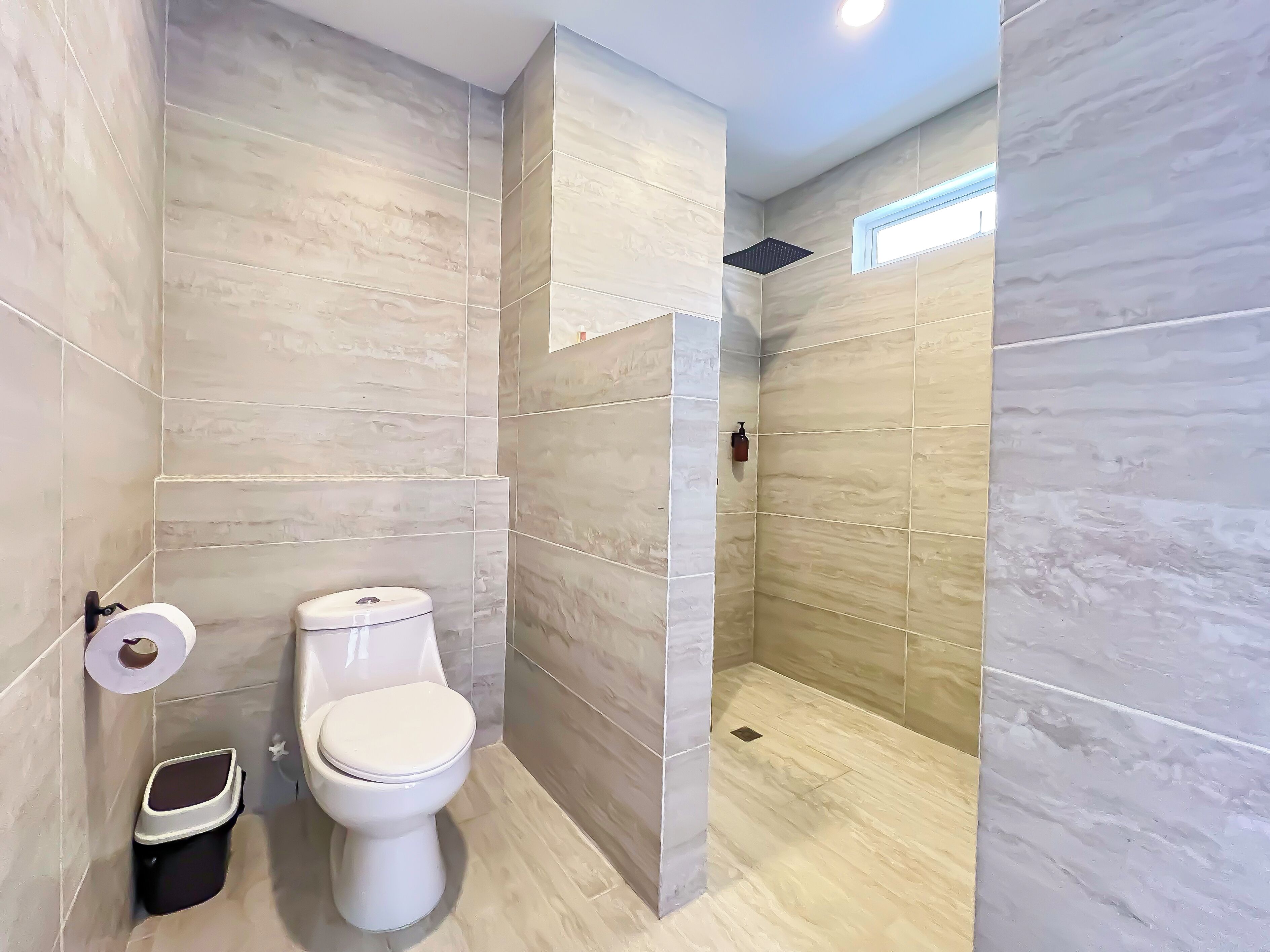 A modern bathroom with a toilet, a trash bin, and a shower area.