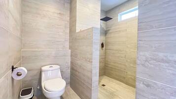 A modern bathroom with a toilet, a trash bin, and a shower area.