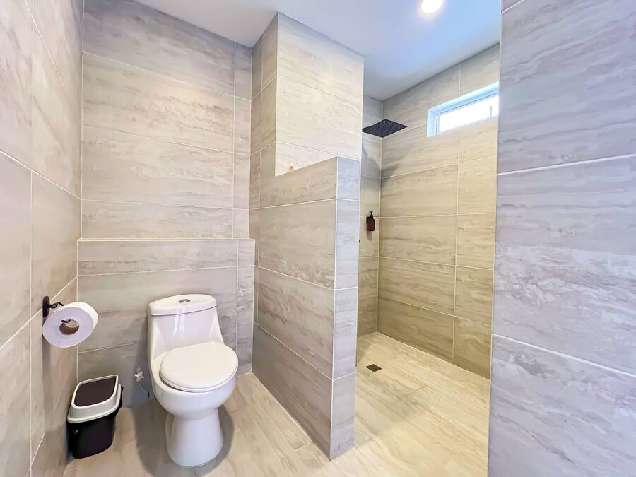 A modern bathroom with a toilet, a trash bin, and a shower area.